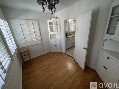 A chandelier hangs over a kitchen island with a sink and a window with shutters.