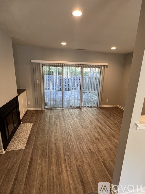 A spacious room with wooden flooring and a sliding glass door leading to a balcony.