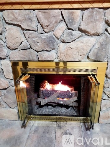 A living room with a stone fireplace and a black leather couch.