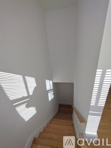 A room with wooden stairs and white walls with sunlight coming through the windows.