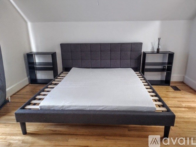 A bed with a grey headboard and a white sheet is in the center of the room.