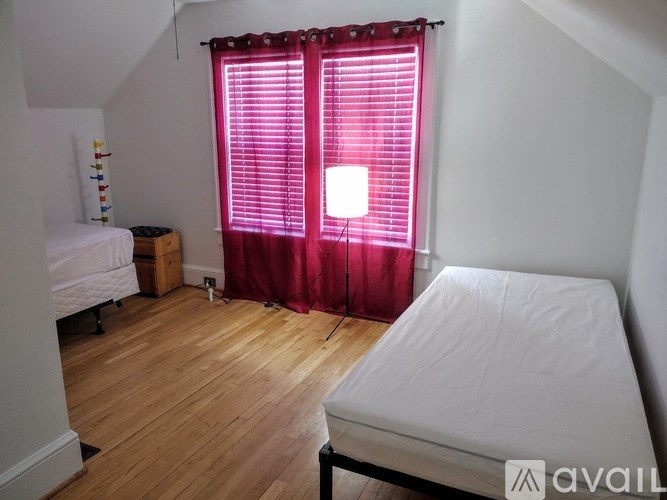 A bedroom with a bed, a window with red curtains, and a wooden floor.