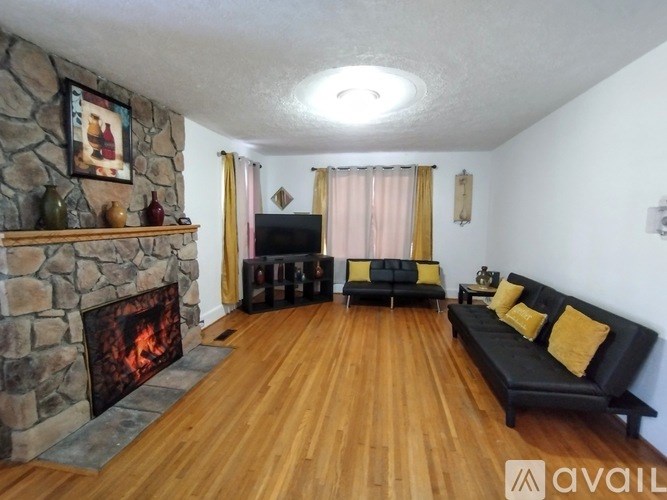 A living room with a stone fireplace and a black couch.