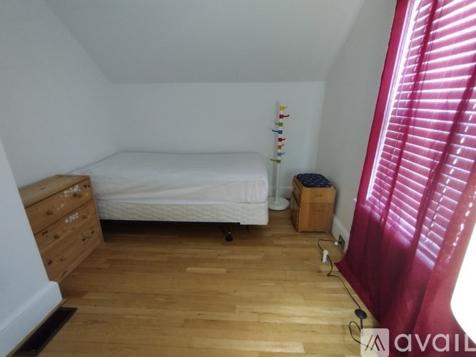 A bedroom with a bed, dresser, and window with red curtains.