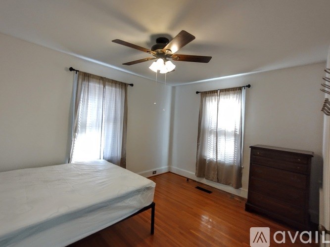 A bedroom with a bed, dresser, and window with curtains.
