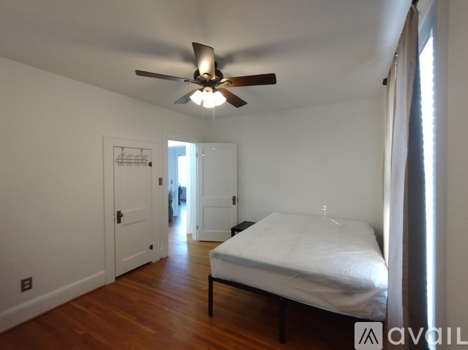 A bedroom with a bed, a ceiling fan, and a door leading to a hallway.