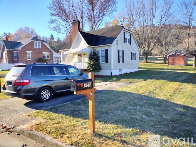 A silver minivan is parked in front of a house with a mailbox that has the number 765 on it.