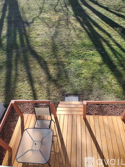 A wooden deck with a table and chairs and a shadow of a tree.