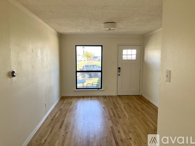 A room with wooden floors and a window showing a view of a street with cars and houses.