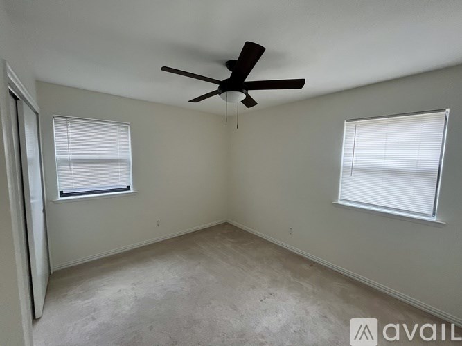 A room with a ceiling fan and two windows.