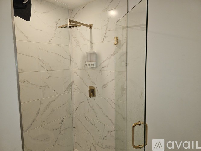 A white marble tiled shower with a gold shower head and faucet.