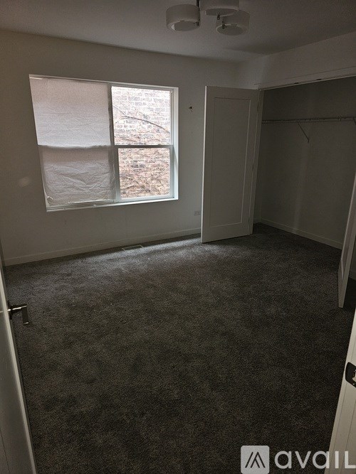 A room with a carpeted floor, a window with a view of bare trees, and a door on the right.