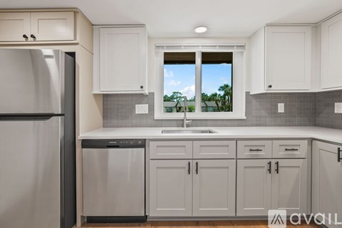 A kitchen with white cabinets and a window overlooking a green landscape.