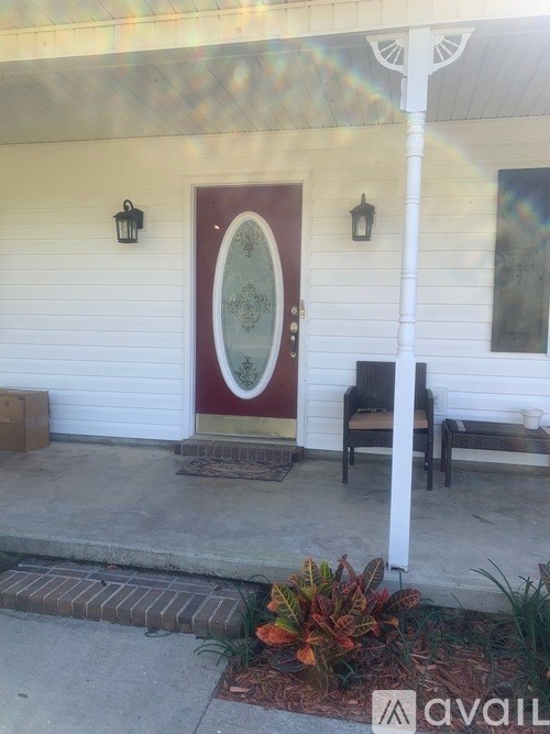 A white house with a red door and a bench on the porch.