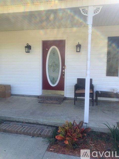 A white house with a red door and a bench on the porch.