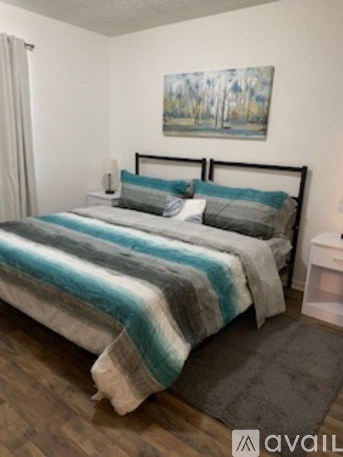 A bedroom with a bed, nightstand, and a painting on the wall.