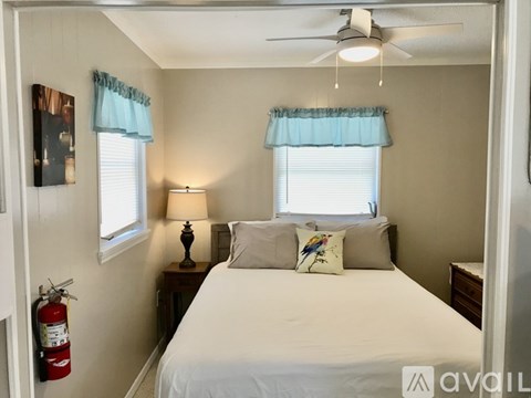 A bedroom with a bed, a nightstand with a lamp, and a fire extinguisher.