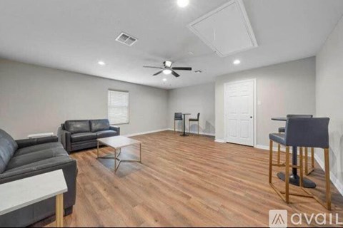 A living room with a black leather couch and a wooden floor.