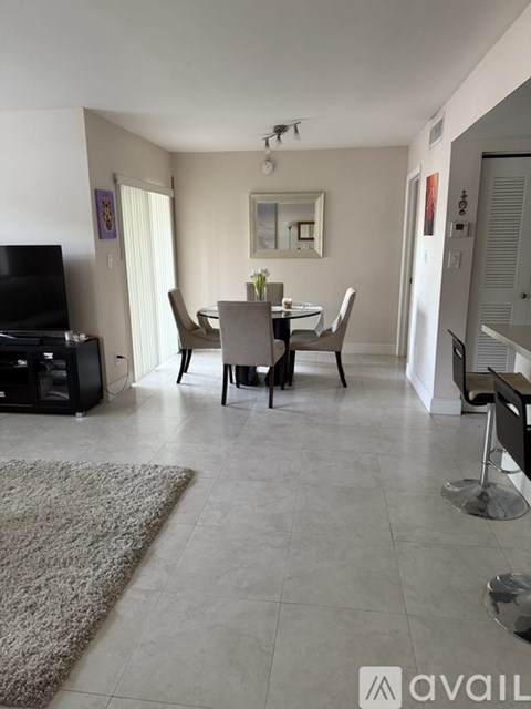 A living room with a grey rug, a black television, and a dining table with chairs.