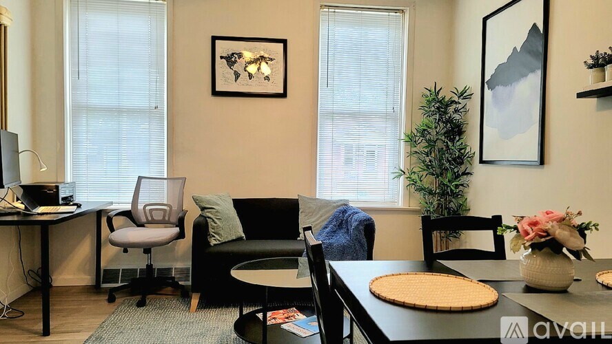 A living room with a black couch, a grey chair, a black table, a plant, and a framed picture on the wall.