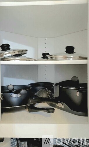A white shelf with black pots and pans on it.