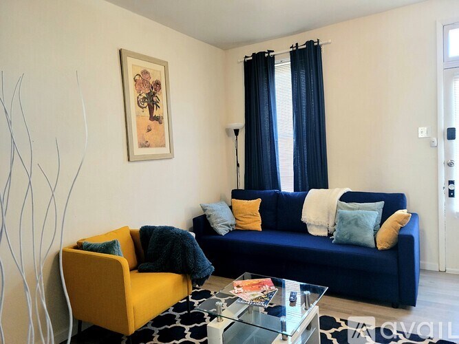 A living room with a blue couch, yellow chair, and a painting on the wall.