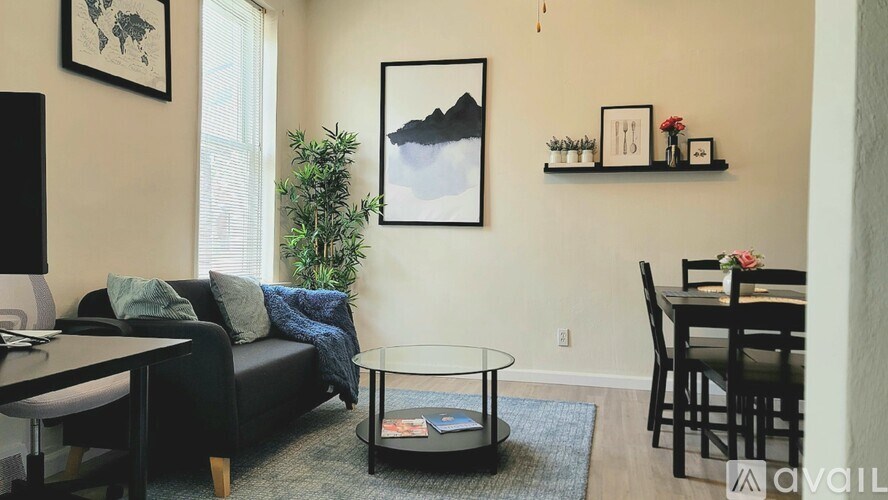 A living room with a black couch, a glass coffee table, and a dining table with chairs.