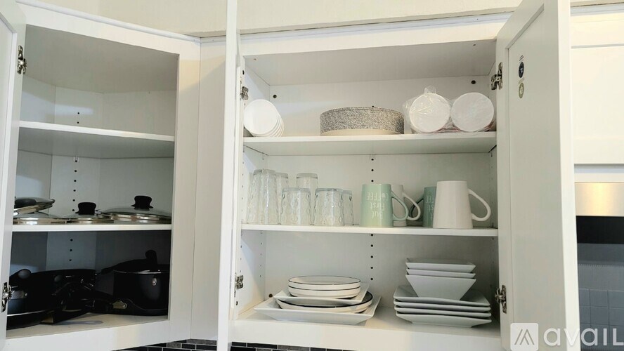 A white kitchen cabinet with plates and cups on the shelves.