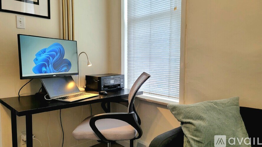A black desk with a laptop, monitor, and a chair in front of a window.