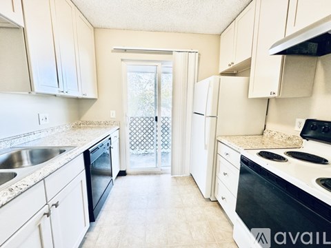 A kitchen with white cabinets and appliances, a sink, and a window with a lattice screen.
