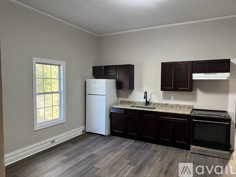 A kitchen with a white refrigerator, dark brown cabinets, and a window with a view of trees.