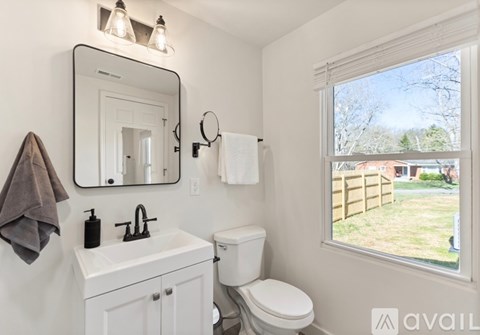 A bathroom with a toilet, sink, mirror, and a window.