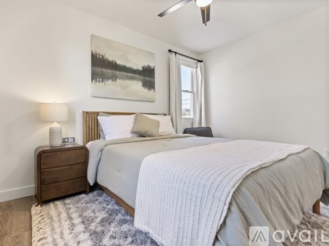 A bedroom with a large bed, a ceiling fan, and a painting on the wall.