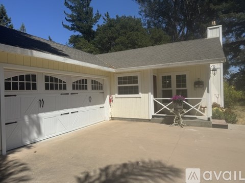 A white house with a garage has a sign that says "available" in front of it.