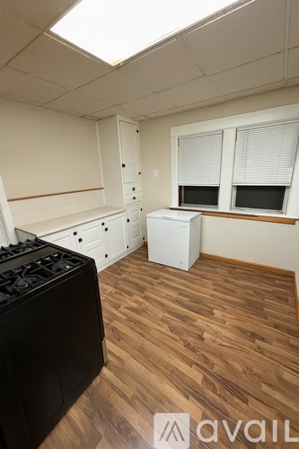 A black stove sits in a kitchen with wooden floors and white cabinets.