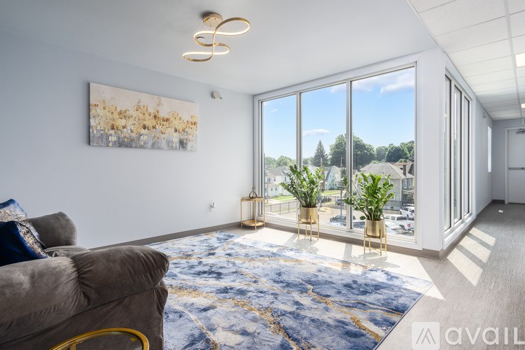 A living room with a grey couch and a large window overlooking a street.