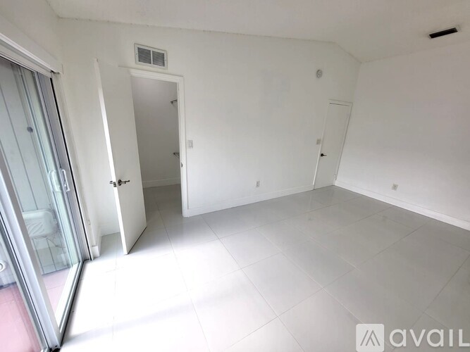 A room with white walls and a glass door leading to a balcony.