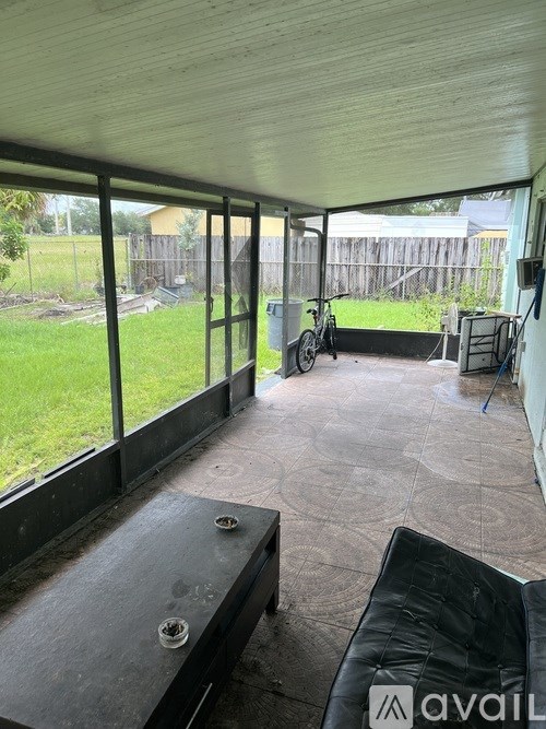 A patio with a black couch and a table with a glass top.