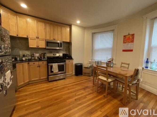 A kitchen with wooden floors and cabinets, a stove, and a dining table with chairs.