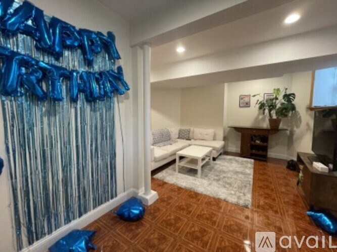 A room with a white sofa and a wooden table is decorated with blue balloons.