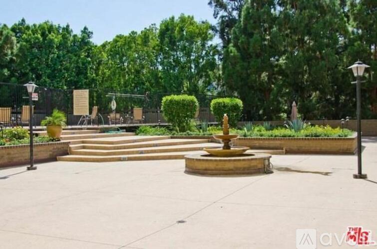 A park with a fountain in the middle of a paved area.
