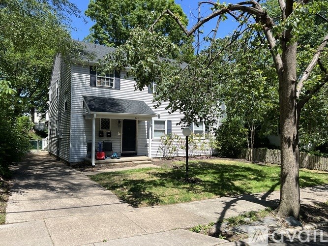 A house with a grey roof and white siding is surrounded by green trees.