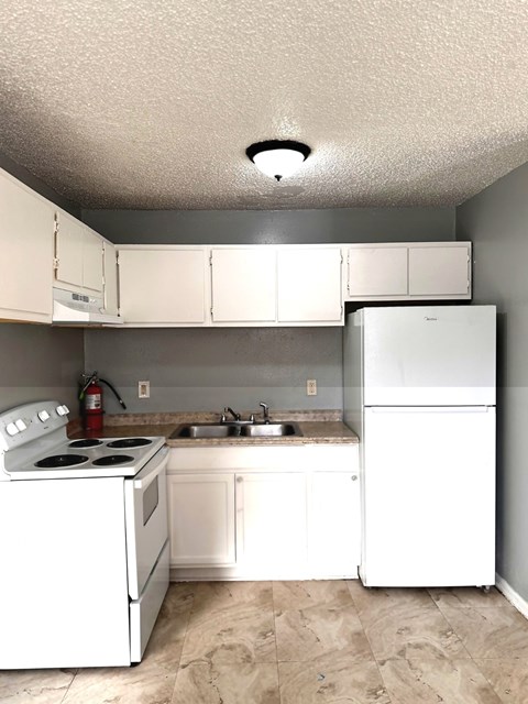 A white kitchen with a stove, sink, and refrigerator.