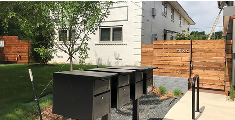 A black mailbox is on the sidewalk in front of a house.