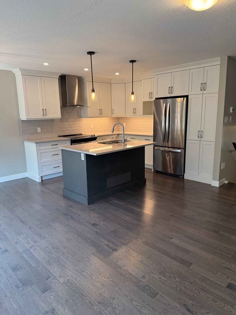 A kitchen with a wooden floor and a stainless steel refrigerator.