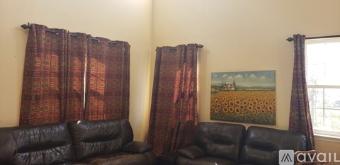 A living room with two black leather couches and a painting of a field of sunflowers.