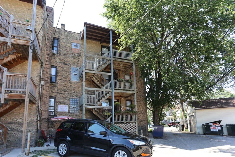 A black car is parked in front of a building with a tree in the background.