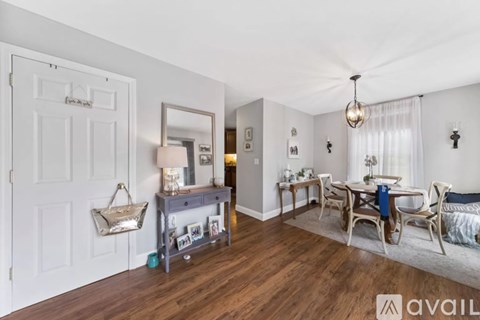 A living room with a white door, a mirror, a table with chairs, and a rug.