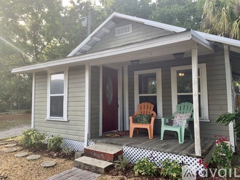 A small house with a red door and two chairs on the porch.