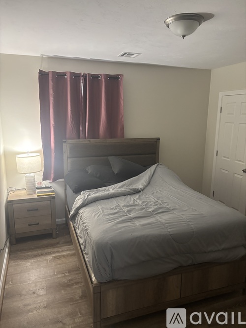 A bedroom with a bed, nightstand, and window with curtains.